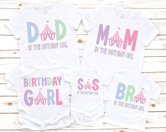 May include: A set of five white t-shirts with colorful text and a circus tent graphic. The shirts say "Dad of the Birthday Girl", "Mom of the Birthday Girl", "Birthday Girl", "Sis of the Birthday Girl", and "Bro of the Birthday Girl".