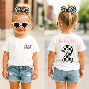 May include: A white t-shirt with a black and white checkered design that says "Too Fast" on the front and a black and white checkered number "2" on the back. The shirt is being worn by a child with a black and white checkered bow in their hair and pink sunglasses.