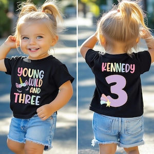 May include: A black t-shirt with a unicorn graphic and the text "Young Wild and Three". The back of the shirt has the name "Kennedy" and the number "3" in rainbow colors.