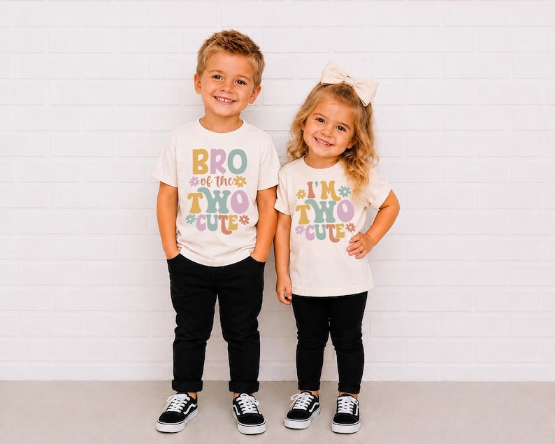 May include: Two off-white short-sleeve t-shirts with black pants and black sneakers. The left shirt features the text BRO of the TWO CUTE with colorful flower graphics. The right shirt features the text I'M TWO CUTE with similar flower graphics.