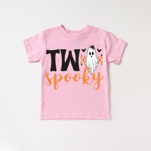 Pu&ograve; includere: T-shirt rosa a maniche corte con le parole "TWo spooky" in nero e arancione. Un fantasma dei cartoni animati con un cappello da strega e pipistrelli &egrave; stampato sul davanti. Perfetto per Halloween.