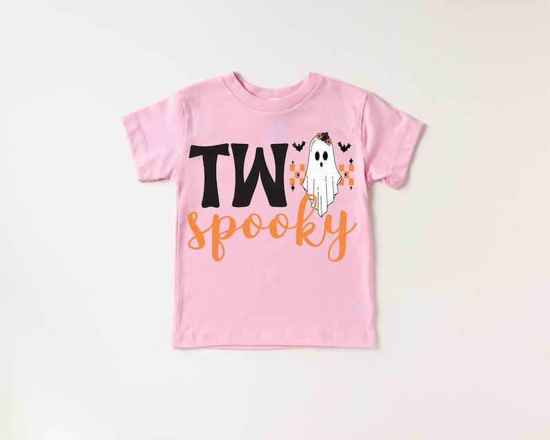 Pu&ograve; includere: T-shirt rosa a maniche corte con le parole "TWo spooky" in nero e arancione. Un fantasma dei cartoni animati con un cappello da strega e pipistrelli &egrave; stampato sul davanti. Perfetto per Halloween.