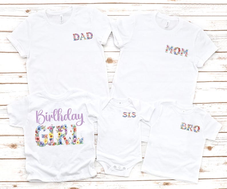 May include: White t-shirts with floral text designs. The shirts include "DAD", "MOM", "SIS", and "BRO" in floral print. A shirt with "Birthday GIRL" in a floral design is also included. The shirts are displayed on a light wood surface.