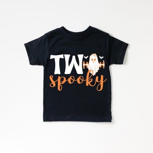 Pu&ograve; includere: T-shirt nera per bambini piccoli con le parole "TWO spooky" in lettere bianche e arancioni. Una grafica di fantasma &egrave; tra le parole "TWO" e "spooky". Due piccoli pipistrelli sono sopra il fantasma.