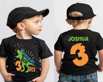 May include: Black t-shirt with a green dinosaur graphic and the text "Birthday Boy Rex" and the number 3. The back of the shirt has the name "Joshua" and the number 3 in orange.