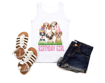 Puede incluir: Camiseta blanca de tirantes con un gráfico de cinco perros de dibujos animados que llevan sombreros de fiesta y flores. El texto "Birthday Girl" está impreso en rosa debajo de los perros. La camiseta se combina con pantalones cortos de mezclilla y sandalias blancas.