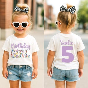 May include: A white short-sleeve t-shirt featuring the text Birthday Girl with floral lettering on the front and the name Sadie with the number 5 in large purple font on the back, paired with blue denim shorts, heart sunglasses, and a bow.