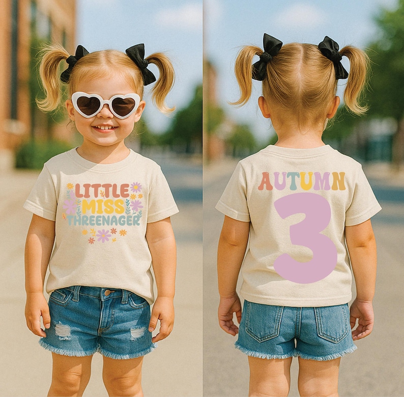 May include: A beige short-sleeved t-shirt featuring the text Little Miss Threenager with colorful floral graphics on the front and the name Autumn with a large number 3 on the back. The shirt is paired with blue denim shorts and heart-shaped sunglasses.