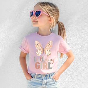 May include: A light pink t-shirt with a watercolour butterfly and the words "Birthday GIRL" in pastel shades. The shirt is worn by a young person wearing heart-shaped sunglasses.