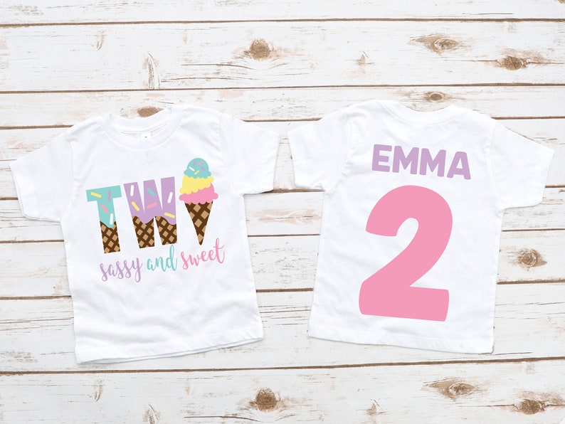 Pu&ograve; includere: Due magliette bianche con un design a forma di cono gelato. La maglietta anteriore dice "TWO sassy and sweet" con un cono gelato. La maglietta posteriore dice "EMMA 2" in rosa.