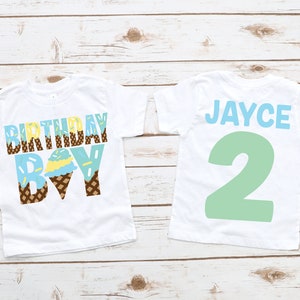 May include: Two white t-shirts with blue and brown ice cream cone designs. The front shirt says "Birthday Boy" and the back shirt says "Jayce 2".