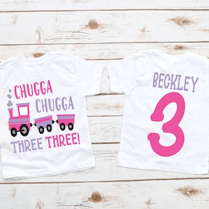 May include: Two white t-shirts with a pink train design and the text "Chugga Chugga Three Three!" on the front and the name "Beckley" and the number "3" on the back.