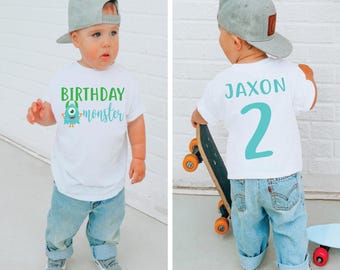 May include: A white t-shirt with a green monster graphic and the text "Birthday monster". The back of the shirt has the name "Jaxon" and the number "2" in teal blue.