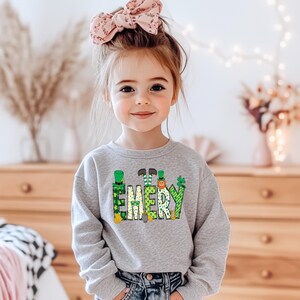 May include: A gray sweatshirt with a green, yellow, and orange design of leprechauns spelling out the name "EMERY".