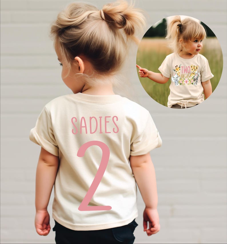 May include: A light beige t-shirt with pink text that says "SADIES 2" on the back. The shirt is being worn by a child.