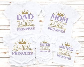 May include: Set of four white t-shirts with purple and gold text and crown designs. The shirts say "Dad of the Birthday Princess", "Mom of the Birthday Princess", "Sister of the Birthday Princess", and "Brother of the Birthday Princess".