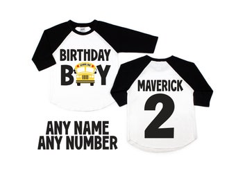 Peut inclure: Deux t-shirts de style baseball, l'un blanc avec des manches noires et l'autre noir avec des manches blanches. Le devant du t-shirt blanc présente un bus scolaire jaune avec le texte "Birthday Boy" en noir. Le dos du t-shirt noir présente le texte "Maverick" et le chiffre "2" en noir.