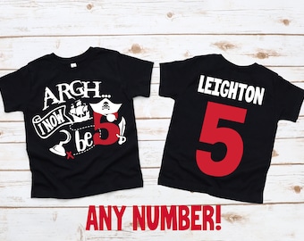 May include: Two black t-shirts with a pirate theme. The front shirt has a white graphic with the text "Argh... I now be 5" and a pirate ship. The back shirt has the text "Leighton 5" in white and red.