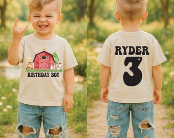 May include: A beige short-sleeve t-shirt featuring a red barn graphic with the text "BIRTHDAY BOY" on the front and the name "RYDER" above the number "3" in large black lettering on the back, paired with light blue distressed denim jeans.