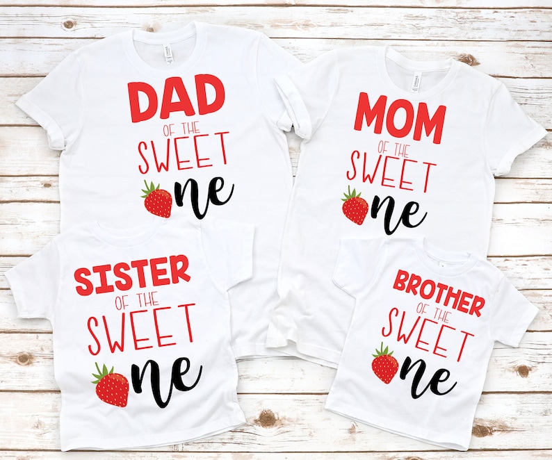 K&ouml;nnte beinhalten: Vier wei&szlig;e T-Shirts mit rotem Text und einer Erdbeergrafik. Die Shirts sagen "Papa vom s&uuml;&szlig;en Kleinen", "Mama vom s&uuml;&szlig;en Kleinen", "Schwester vom s&uuml;&szlig;en Kleinen" und "Bruder vom s&uuml;&szlig;en Kleinen".