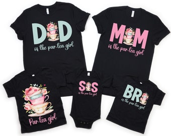 Op de afbeelding: Een set van vijf zwarte t-shirts met een theekopontwerp en tekst die luidt "DID of the par-tea girl", "MOM of the par-tea girl", "SIS of the par-tea girl", "BR of the par-tea girl", en "Par-tea girl".