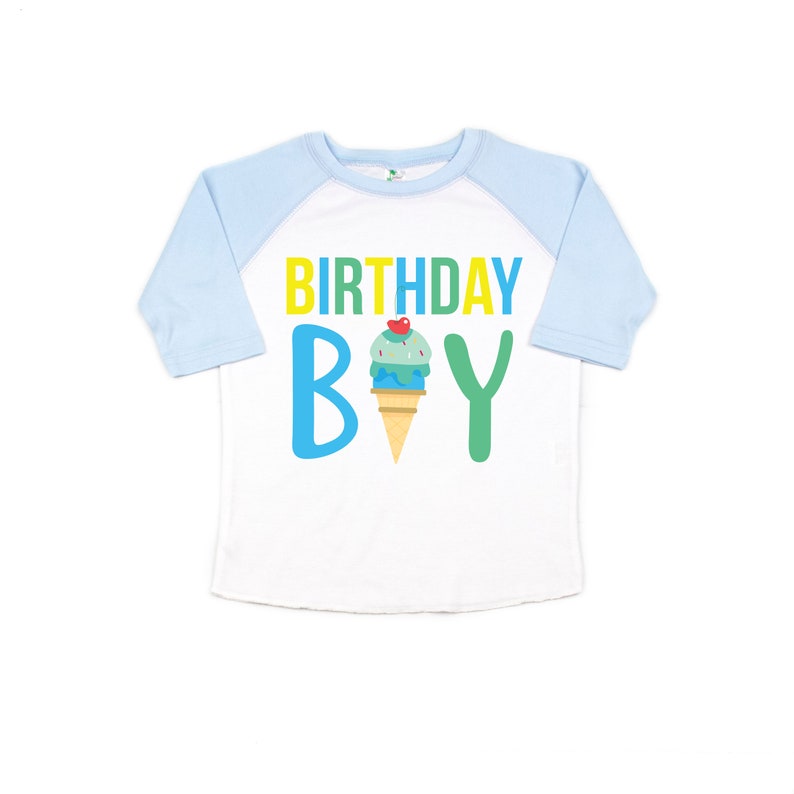 May include: White and light blue baseball tee shirt with a yellow, green, and blue graphic that says "Birthday Boy" with an ice cream cone in the middle.