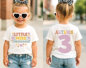 May include: A white short-sleeved t-shirt featuring the text Little Miss Threenager with colourful floral graphics on the front and the name Autumn with the number 3 in large lavender font on the back, paired with blue denim shorts.