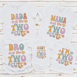 May include: Five white short-sleeved shirts and one white baby bodysuit featuring colorful retro-style typography and flower icons. The text reads DADA OF THE TWO CUTE, MAMA OF THE TWO CUTE, BRO OF THE TWO CUTE, SISSY OF THE TWO CUTE, and I'M TWO CUTE.