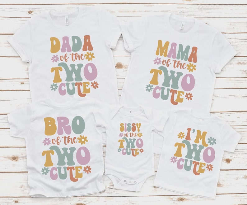 May include: Five white short-sleeved shirts and one white baby bodysuit featuring colorful retro-style typography and flower icons. The text reads DADA OF THE TWO CUTE, MAMA OF THE TWO CUTE, BRO OF THE TWO CUTE, SISSY OF THE TWO CUTE, and I'M TWO CUTE.