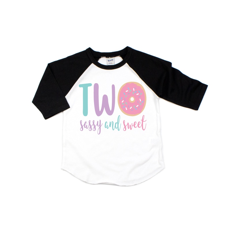 May include: A white and black baseball tee shirt with a pink donut and the text "TWO sassy and sweet".
