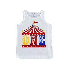 Puede incluir: Camiseta blanca de tirantes con un gr&aacute;fico de carpa de circo roja, amarilla y azul y la palabra "ONE" en letras grandes. La carpa tiene una cubierta a rayas rojas y blancas y banderas azules y blancas.