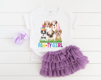 Puede incluir: Camiseta blanca con un gráfico de cinco perros con sombreros de fiesta y el texto "PAW-TY GIRL". La camiseta se combina con una falda de tul morada.