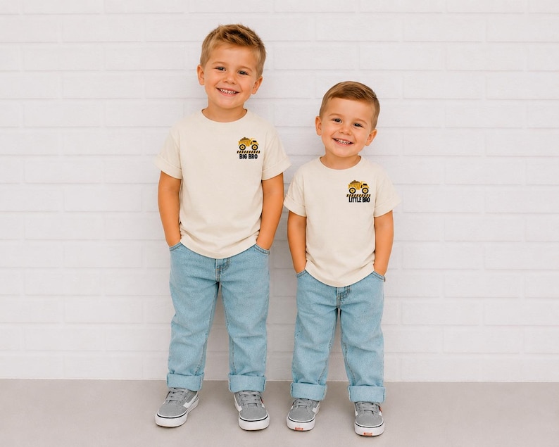May include: Two cream-colored short-sleeve t-shirts with light blue jeans. The left shirt features a yellow construction truck graphic with the text BIG BRO. The right shirt features a yellow construction truck graphic with the text LITTLE BRO.