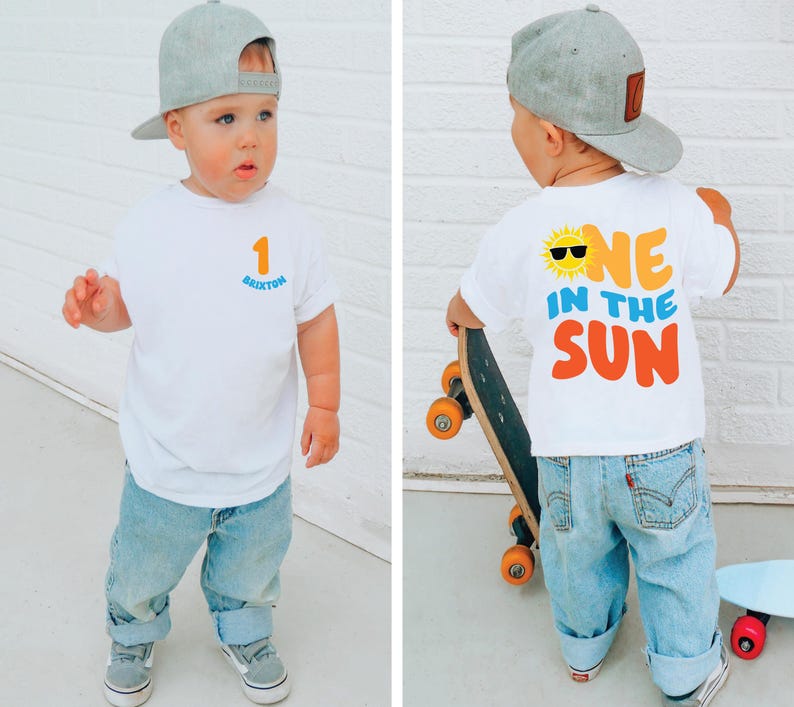 May include: A white short-sleeve t-shirt featuring a small orange number 1 and the name Brixton in blue on the front. The back displays a yellow sun graphic with black sunglasses and the text ONE IN THE SUN in orange and blue lettering.