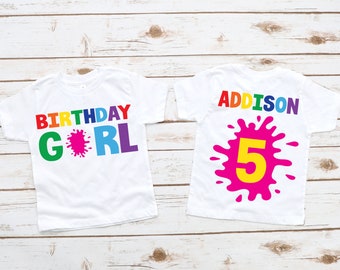 May include: Two white t-shirts with a rainbow paint splatter design. One shirt says "Birthday Girl" and the other says "Addison" with the number "5" in a yellow paint splatter.