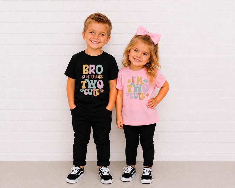 May include: A black t-shirt with the text BRO of the TWO CUTE and a pink t-shirt with the text I'M TWO CUTE, both featuring colorful retro-style lettering and flower graphics. The black shirt is paired with black pants, and the pink shirt is paired with black pants and a pink hair bow.