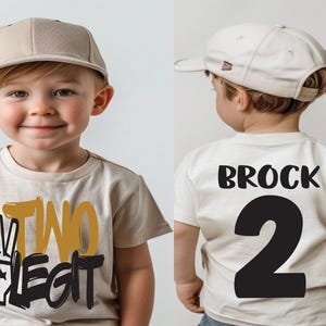 Pu&ograve; includere: Una maglietta beige con la scritta "TWO LEGIT" e un simbolo di pace. Il retro della maglietta ha il nome "BROCK" e il numero "2" stampati in nero. Il bambino indossa un berretto da baseball beige.