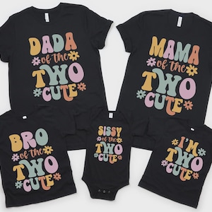 May include: A set of five black t-shirts and one black bodysuit featuring colorful retro-style text and flower graphics. The shirts display phrases including DADA OF THE TWO CUTE, MAMA OF THE TWO CUTE, BRO OF THE TWO CUTE, SISSY OF THE TWO CUTE, and I'M TWO CUTE.