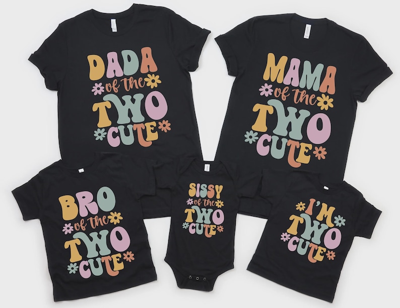 May include: A set of five black t-shirts and one black bodysuit featuring colorful retro-style text and flower graphics. The shirts display phrases including DADA OF THE TWO CUTE, MAMA OF THE TWO CUTE, BRO OF THE TWO CUTE, SISSY OF THE TWO CUTE, and I'M TWO CUTE.