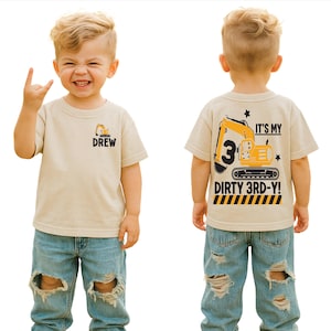May include: A beige t-shirt with a construction theme. The front of the shirt has the name "DREW" and a small excavator graphic. The back of the shirt says "IT'S MY DIRTY 3RD-Y!" with a large number 3 and an excavator graphic.