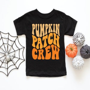 May include: Black t-shirt with the text "PUMPKIN PATCH CREW" in orange and tan lettering. The shirt is surrounded by decorative pumpkins and a spider web. A fun Halloween-themed design.