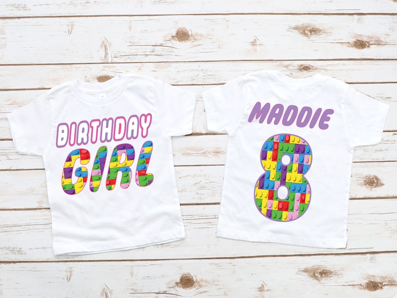 May include: Two white t-shirts with a birthday theme. The first shirt says "Birthday Girl" in pink letters with a colourful Lego block design. The second shirt has a large number 8 made of Lego blocks and the name "Maddie" in purple letters.