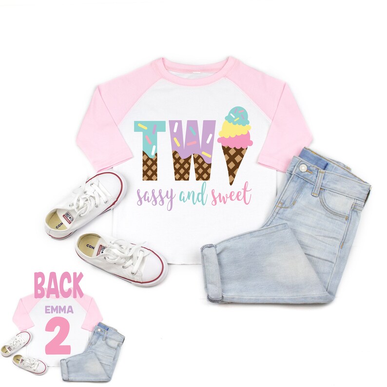 Pu&ograve; includere: Una maglietta da baseball bianca e rosa con il testo "TWO sassy and sweet" e una grafica a forma di cono gelato. La parte posteriore della maglietta ha il numero "2" in rosa.