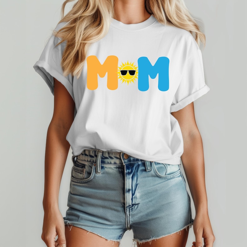 May include: A white short-sleeve t-shirt featuring the text MOM in a bold, rounded font. The letter O is replaced by a yellow sun graphic wearing black sunglasses. The M letters are orange and blue, respectively, printed on the chest area.