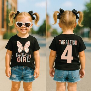 May include: A black t-shirt featuring a butterfly design and the text "birthday GIRL" in pink. The back of the shirt displays the name "TARALEIGH" and the number "4" in pink. The child is wearing denim shorts and heart-shaped sunglasses.