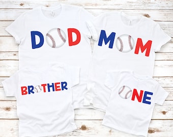 May include: White t-shirts with baseball-themed designs. The shirts feature the words "DAD", "MOM", "BROTHER", and "ONE" in blue and red, with a baseball graphic in the center of each word. Family apparel.