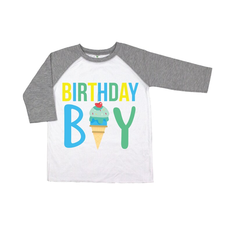 May include: A white and grey raglan t-shirt with the text "BIRTHDAY BOY" in yellow, blue, and green letters. An ice cream cone with a cherry on top is in the middle of the text.