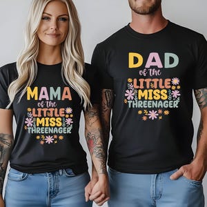 May include: Two black short-sleeve t-shirts featuring colorful floral graphics and text. One shirt displays 'MAMA of the LITTLE MISS THREENAGER' and the other displays 'DAD of the LITTLE MISS THREENAGER' in a mix of pastel and bold lettering.
