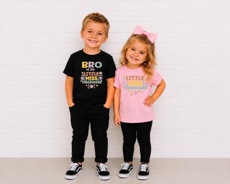 May include: A black t-shirt with the text BRO OF THE LITTLE MISS THREENAGER and a pink t-shirt with the text LITTLE MISS THREENAGER, both featuring colorful floral graphics. The shirts are paired with black pants and black sneakers.