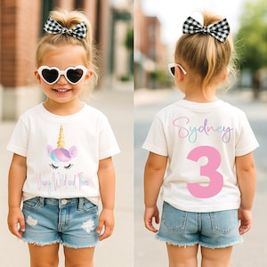 May include: A white short-sleeve t-shirt featuring a unicorn graphic with a gold horn and the text Young Wild and Three on the front, and the name Sydney with the number 3 in pink on the back, paired with blue denim shorts and a hair bow.